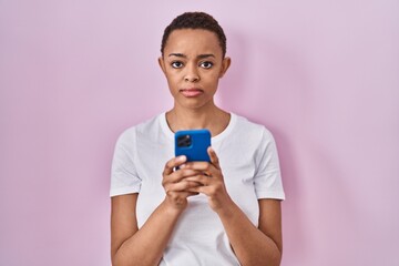 Beautiful african american woman using smartphone relaxed with serious expression on face. simple and natural looking at the camera.