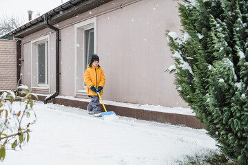 Close-up of a woman cleaning and clearing snow in front of the house on a sunny and frosty day. Cleaning the street from snow on a winter day. Snowfall, and a severe snowstorm in winter.