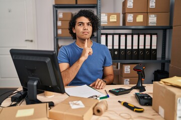 Hispanic man with curly hair working at small business ecommerce thinking concentrated about doubt with finger on chin and looking up wondering