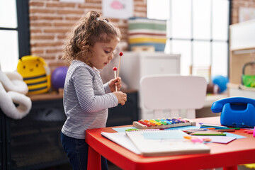 Adorable caucasian girl playing xylophone standing at kindergarten