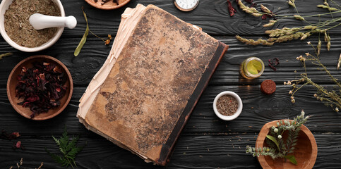 Old book and ingredients for preparing potions on dark alchemist's table