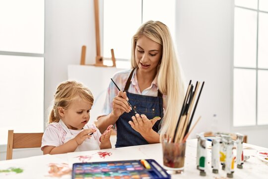 Mother and daughter smiling confident painting palm hands at art studio