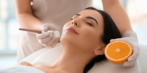 Obraz na płótnie Canvas Cosmetologist applying mask with vitamin C onto woman's face in beauty salon