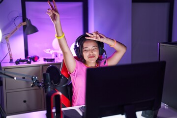 Young hispanic woman streamer playing video game dancing at gaming room