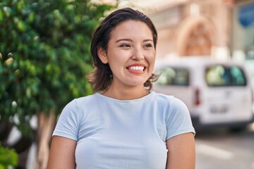 Young hispanic woman smiling confident looking to the side at street