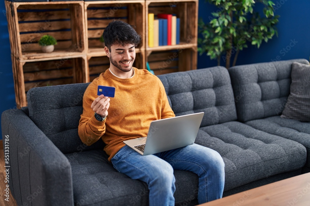Canvas Prints young hispanic man using laptop and credit card sitting on sofa at home - Canvas Prints