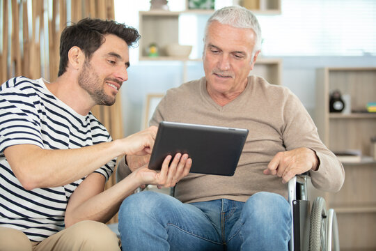 smiling handsome man showing tablet to man in wheelchair