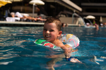 A little boy swims in a beautiful blue pool in an inflatable circle.	