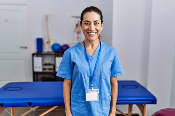 Young hispanic woman wearing physiotherapist uniform standing at clinic with a happy and cool smile on face. lucky person.