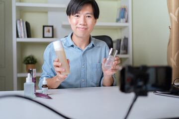 Young adult Asian beauty video blogger man filming, online live streaming his video blog about male cosmetic, male skincare. Guy looking camera to show new skin care for men product, teaching make up.