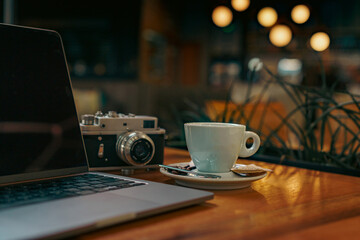 Photo of a cup of coffee with late art drawn on it, laptop notes and a vintage camera on the table next to the coffee cup