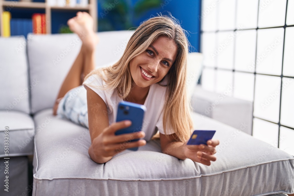 Sticker young blonde woman using smartphone and credit card lying on sofa at home