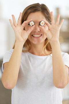 smiling young woman holding sushi in front of eyes