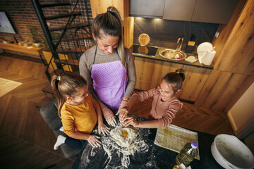 Attractive young mother and adorable daughters kneading dough in kitchen, they are laughing and enjoying their time together
