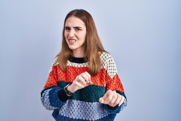 Young hispanic girl standing over blue background disgusted expression, displeased and fearful...