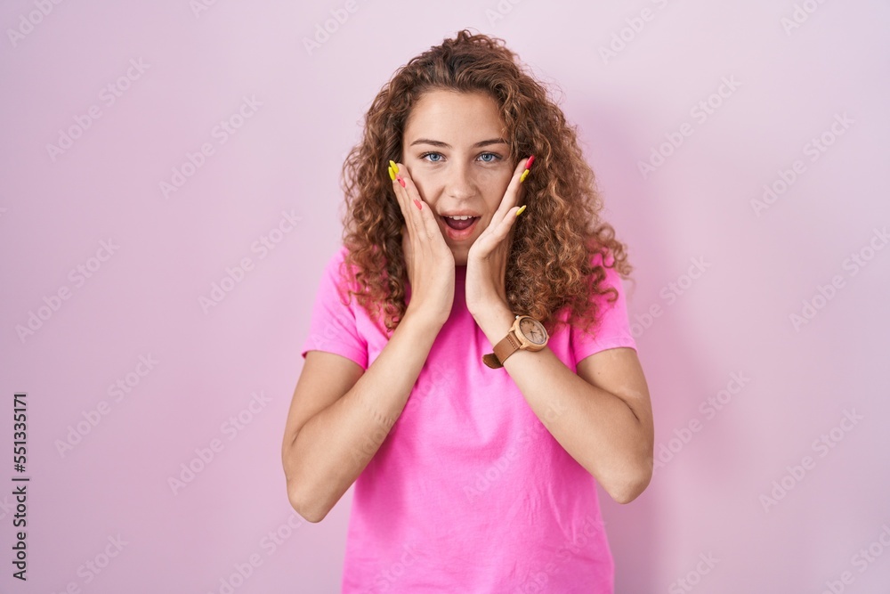 Poster Young caucasian woman standing over pink background afraid and shocked, surprise and amazed expression with hands on face