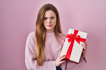 Young caucasian woman holding gift skeptic and nervous, frowning upset because of problem. negative person.