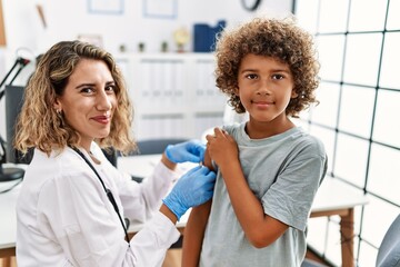 Mother and son wearing doctor uniform putting band aid on child arm at clinic