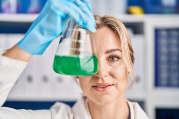 Young blonde woman scientist holding test tube over eye at laboratory