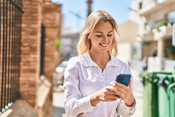 Young blonde woman smiling confident using smartphone at street