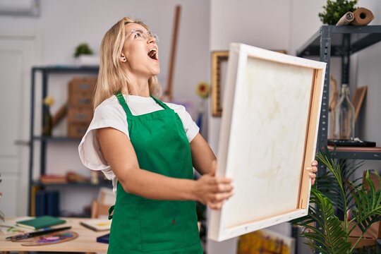 Young caucasian woman looking at canvas angry and mad screaming frustrated and furious, shouting with anger looking up.
