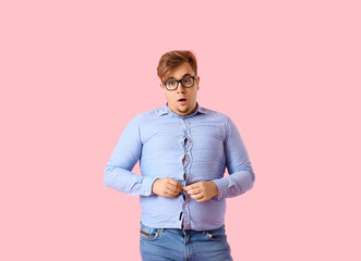 Young overweight man in tight shirt on pink background