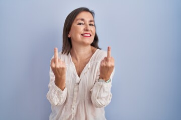 Middle age hispanic woman standing over blue background showing middle finger doing fuck you bad...