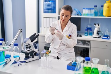 Middle age woman scientist holding flower with tweezer at laboratory