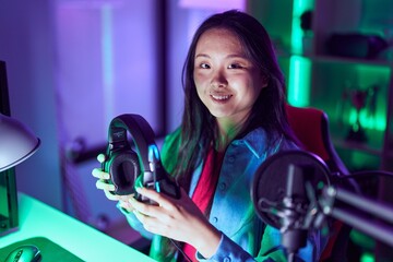 Young chinese woman streamer using computer holding headphones at gaming room