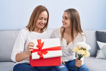 Two women mother and daughter surprise with birthday gift and flowers at home