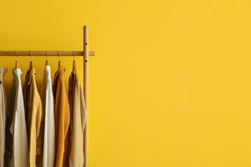Rack with trendy clothes near yellow wall