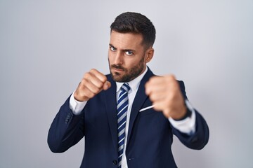 Handsome hispanic man wearing suit and tie punching fist to fight, aggressive and angry attack, threat and violence