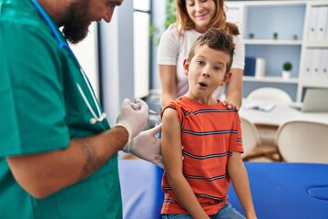 Young kid getting vaccine at doctor clinic scared and amazed with open mouth for surprise, disbelief face