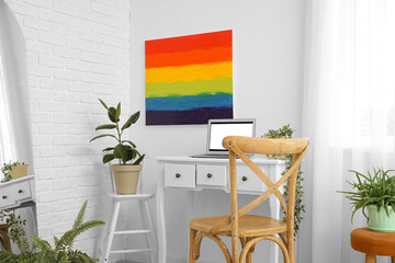 Workplace with laptop and painting of LGBT flag on light wall in room
