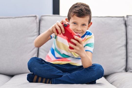 Blond child playing video game sitting on sofa at home