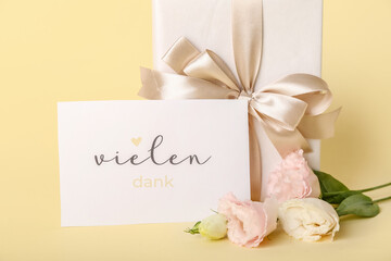 Card with text VIELEN, gift box and eustoma flowers on color background