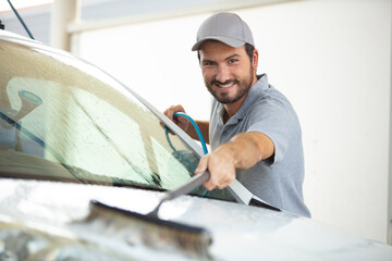 portrait of confident male worker washing red car at garage