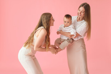 Happy lesbian couple with their little baby on pink background