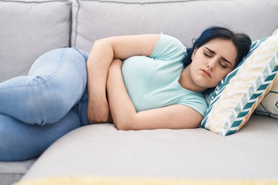 Young caucasian woman suffering for menstrual pain lying on sofa at home