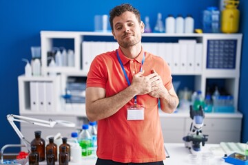 Young hispanic man working at scientist laboratory smiling with hands on chest with closed eyes and grateful gesture on face. health concept.