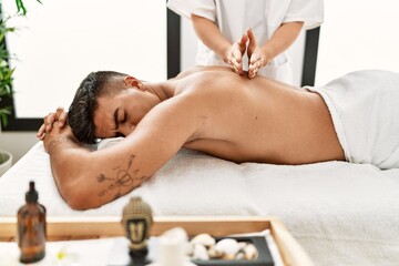 Obraz na płótnie Canvas Young hispanic man relaxed having back massage at beauty center