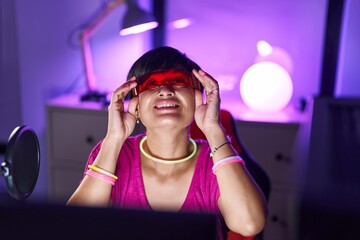 Middle age chinese woman streamer playing video game using virtual reality glasses at gaming room