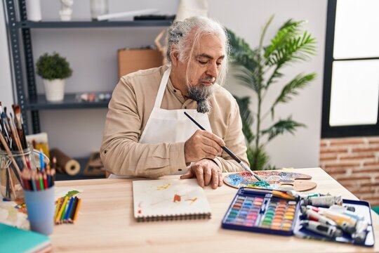 Middle age grey-haired man artist drawing on notebook with relaxed expression at art studio