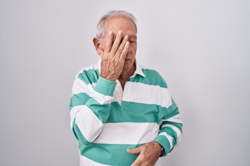Senior man with grey hair standing over white background with sad expression covering face with...