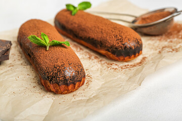 Baking paper with tasty chocolate eclairs on table, closeup