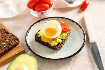 Plate of delicious toast with boiled egg and avocado on light tile
