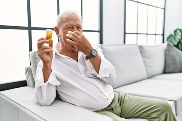 Senior man holding pills smelling something stinky and disgusting, intolerable smell, holding...