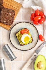 Plate of delicious toast with boiled egg, avocado and tomatoes on light tile