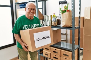 Senior man wearing volunteer uniform holding donations package at charity center