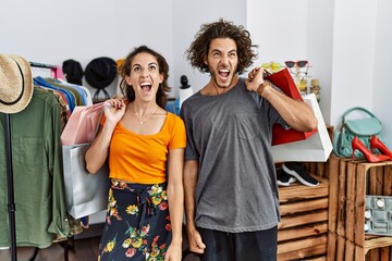 Young hispanic couple holding shopping bags at retail shop angry and mad screaming frustrated and furious, shouting with anger. rage and aggressive concept.